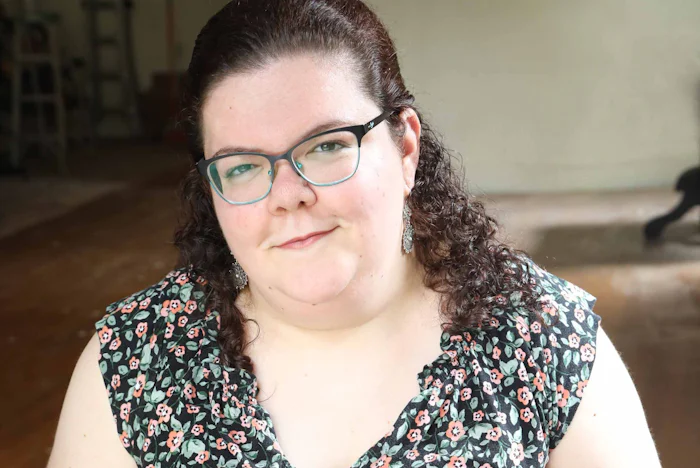 A head and shoulder portrait of Emily Ladau, a white woman with brown curly hair and glasses, wearing a flowered shirt. 