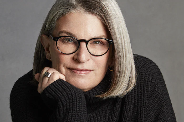 A portrait of Sally Susman, a white woman with glasses, resting her chin in her hand.