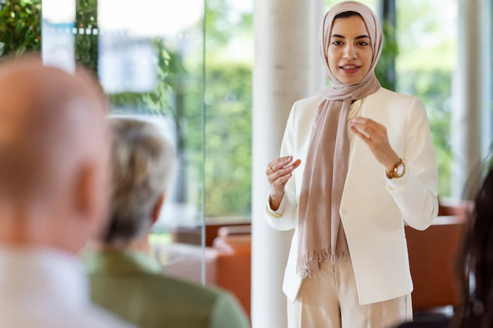 Young middle eastern businesswoman giving a speech in a business seminar. Muslim woman wearing headscarf addressing the audience in a business conference.